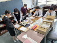 点字封筒の作り方を説明する女子生徒と真剣に聞く大学生