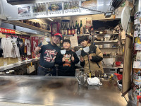 お好み焼き屋さんの店主と児童二人で、お店の中で写真を撮っている。