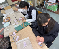 さをり織りのストラップを袋に入れる２名の女子生徒