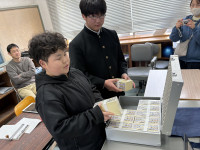租税教室で札束のレプリカに触れる小学部児童と中学部生徒